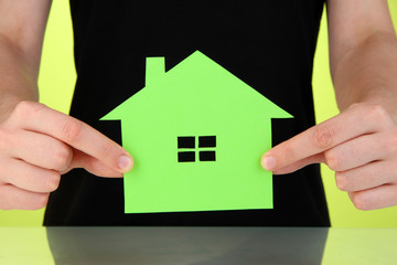 Paper house in hand on green background