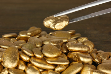 Tweezers holding golden stone on wooden background