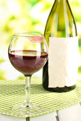 Glass of wine and bottle on table on nature background