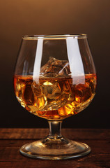 Brandy glass with ice on wooden table on brown background