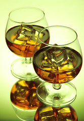 Brandy glasses with ice on green background