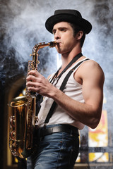 Fototapeta na wymiar Creative soul. Handsome young men in hat playing sax with a smo