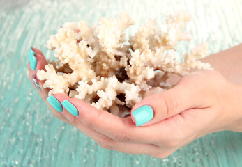 Beautiful woman hands with blue manicure holding coral,