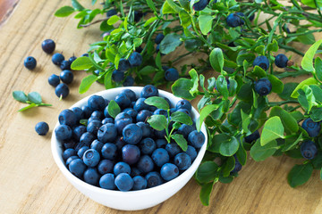 Bunch of fresh blueberry in the white bowl on wooden background © istetiana