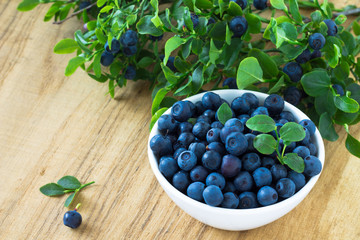 Bunch of fresh blueberry in the white bowl on wooden background