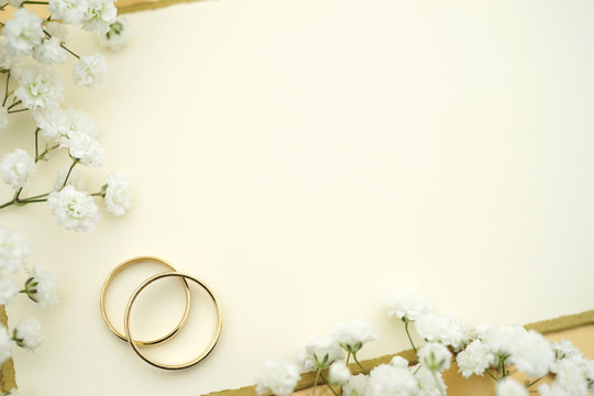 Elegante Hochzeitseinladung mit Eheringen aus Gold, einer Karte mit Textfreiraum und weissen Blumen. Copy space