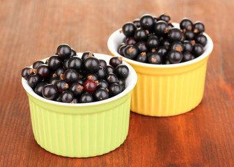Fresh black currant in bowls on wooden background