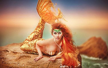 Beautiful fashionable mermaid sitting on a rock by the sea