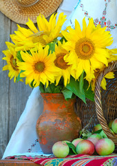 Obraz premium Vase with sunflowers and by a basket with apples