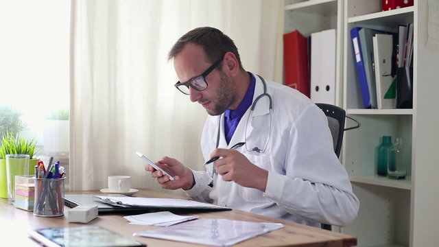Male doctor with smartphone and documents in office