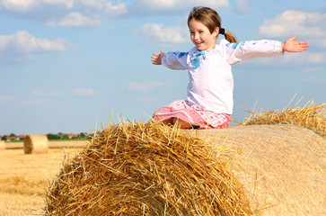 Naklejka na ściany i meble small rural girl on the straw after harvest field with straw bal