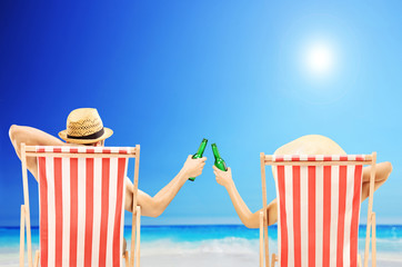 Man and woman relaxing on a beach and cheering with beers