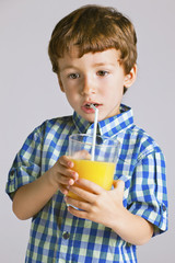 Child with plaid shirt drinking a fresh orange juice.