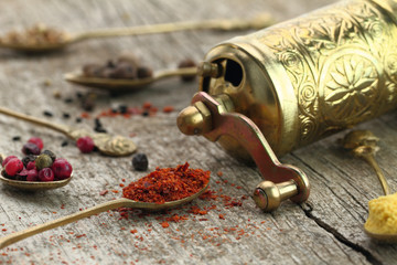 Old spoons with spices and pepper grinder on wooden background