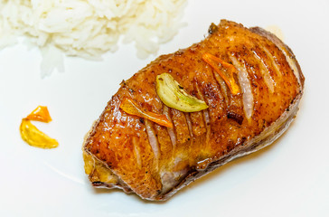 A tasty cooked goose's magret (filet) with orange, garlic and rice on a white plate