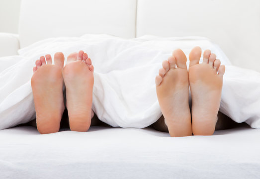 Close-up of couple's feet sleeping on bed