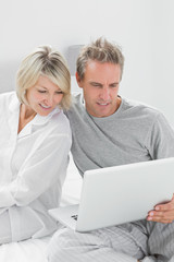 Couple using laptop sitting on bed