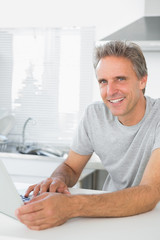 Smiling man using laptop in kitchen