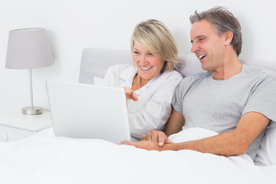 Happy couple using laptop in bed