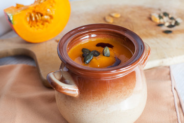 Pumpkin vegetable cream soup in brown bowl with piece pumpkin