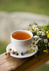 cup of tea, wild strawberry, bouquet of wild flowers on a wooden