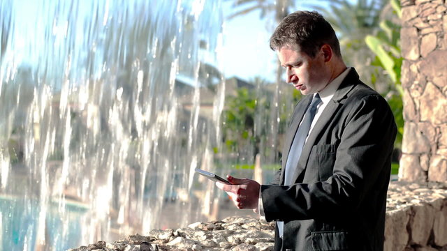 Businessman relaxing by the waterfall and taking photo by cellph