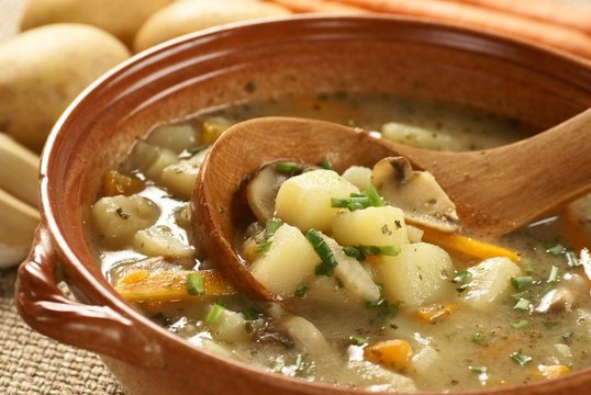 Detail of bowl with potato soup and wooden ladle