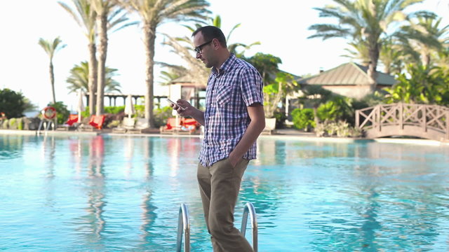 Young man walking by the poolside with cellphone