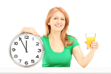 Mature woman holding a wall clock and glass of orange juice on a