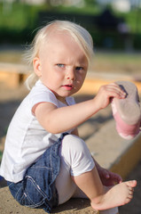 Toddler put on her shoes near sandbox