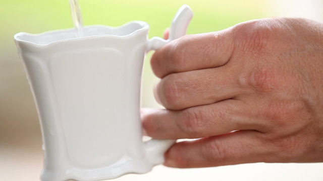 Hand holding porcelain mug and pouring mineral water in spa.