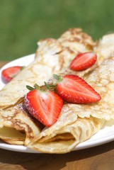 Sweet crepes with strawberries on garden table