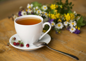 cup of tea, wild strawberry, bouquet of wild flowers on a wooden