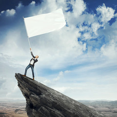 Man with blank flag standing on the top of a rock