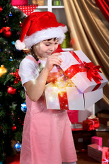 Fototapeta na wymiar A little girl opens a gift in festively decorated room