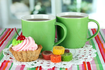 Cups of tea with cake and candy on table in room