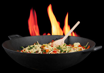Noodles with vegetables on wok on fire background