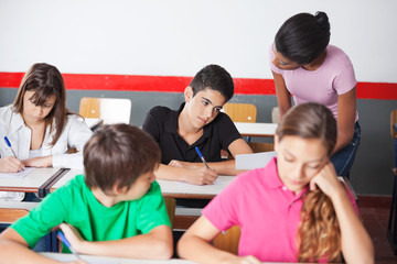 Teacher Assisting Teenage Schoolboy During Examination