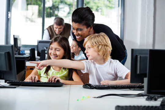 Teacher Assisting Boy Pointing On Computer In Lab - Powered by Adobe