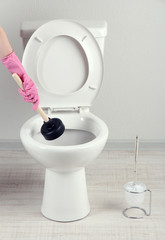 Woman uses a plunger to unclog a toilet bowl in a bathroom