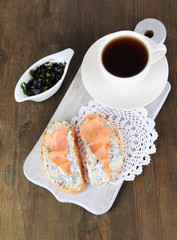 Fish sandwiches and cup of tea on cutting board on wooden table