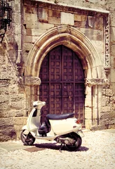 Foto op Plexiglas Scooter Witte vintage scooter in de buurt van middeleeuwse poort