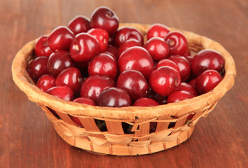 Cherry berries in wicker basket on wooden table close-up