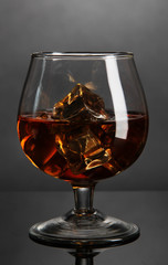 Brandy glass with ice on grey background