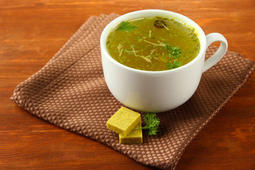 Cup of soup with bouillon cubes on wooden background