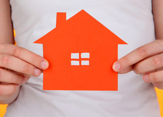 Fototapeta na wymiar Paper house in hands on orange background