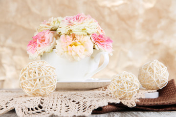 Roses in cup on napkins on  wooden table on beige background