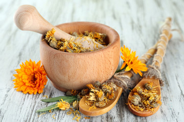 Fresh and dried calendula flowers in mortar on wooden