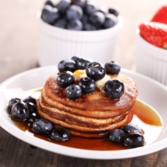 Stack of pancakes with fruits and maple syrup.