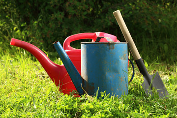 Old watering cans and shovel on grass